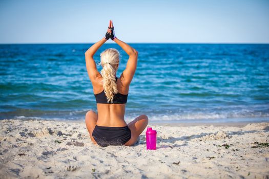beautiful young woman sitting in yoga pose at the beach 