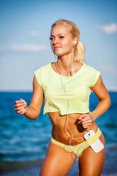 Woman running with earphones on sea background. Caucasian beautiful fitness girl working out on summer