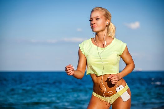 Woman running with earphones on sea background. Caucasian beautiful fitness girl working out on summer