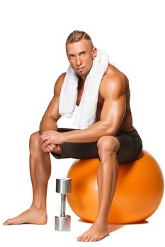 Shaped and healthy body man with a white towel around his neck sitting on fitness ball isolated on white background