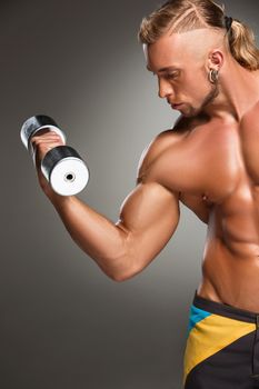 Attractive male body builder with dumbbell on gray background.