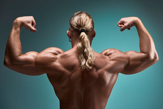 back view of torso of attractive male body builder on blue background.