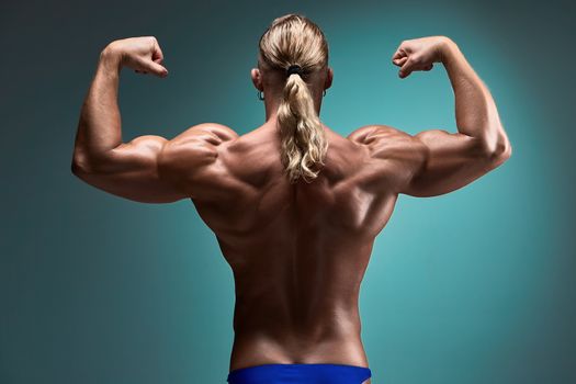 back view of torso of attractive male body builder on blue background.