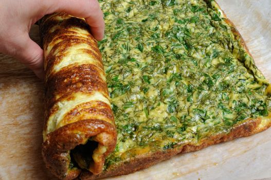 Hand wraps scrambled eggs with herbs in a roll