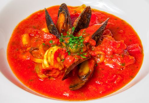 Close up of red seafood soup with mussels on a white plate