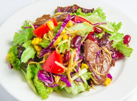 Salad with beef, red beans, corn on the sour-sweet sauce on a white plate