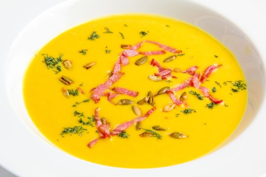 Closeup yellow pumpkin soup with seeds in a white plate