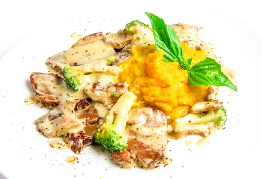 Roast pork with broccoli, mushrooms, cream sauce, potato and pumpkin puree on white plate