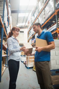 Delivery man passing parcel to warehouse manager in warehouse