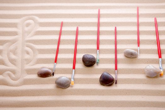 Festive music at the beach background concept with notes of waterworn pebbles and red paintbrushes overlying a score of alternating rows of colored sand with a hand drawn G clef in an artistic design