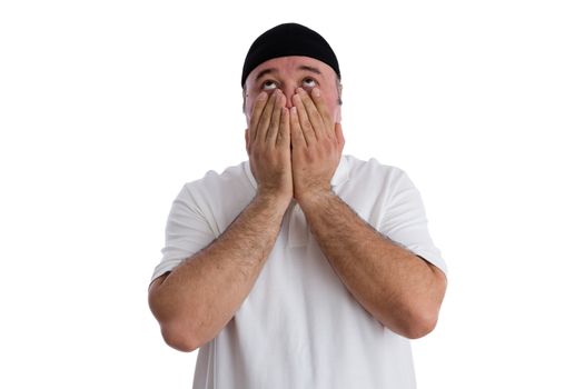Man realising the consequences of his actions looking up to God with an aghast expression seeking help, isolated on white with him covering his cheeks with his hands - What have I done