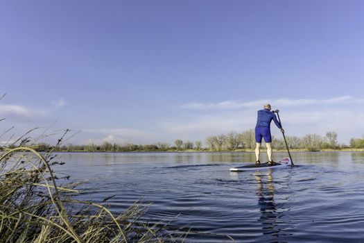 Senior male on stand up paddling (SUP) board. Early spring on calm lake in Fort Collins, Colorado..