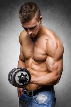 Young man with well trained body, biceps, abs and pecs holds a dumbbell