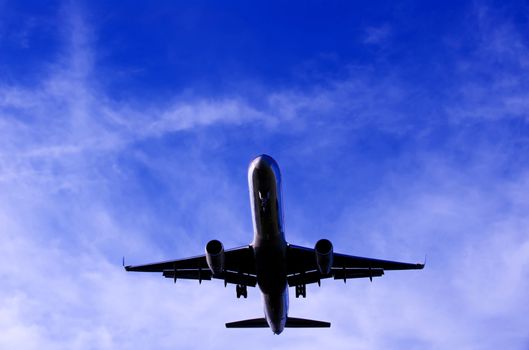 Image of the bottom of a plane flying overhead against deep blue sky