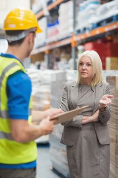 Worker with clipboard speaking with his manager in warehouse