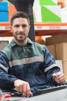 Smiling driver operating forklift machine in warehouse