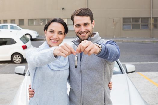 Young couple smiling holding new key outside their car