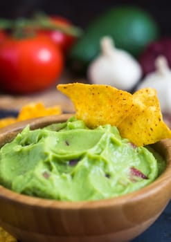 Guacamole in Wooden Bowl with Tortilla Chips and Ingredients Close Up