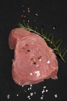 Raw tuna steak with fresh rosemary herb, salt flakes and colorful peppercorns isolated on black background top view. Culinary healthy seafood eating.