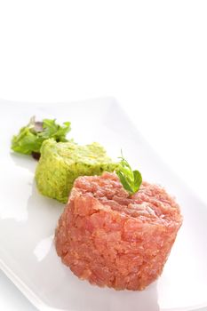 Delicious salmon tartare with fresh salad on white tray isolated on white background. Healthy seafood eating.