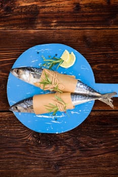 Delicious fresh mackerel fish on wooden kitchen board with lemon, rosemary and salt flakes on brown vintage textured wooden background. Culinary healthy seafood cooking.
