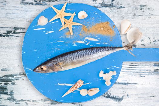 Delicious fresh fish on wooden kitchen board with sea shells on white textured wooden background. Culinary healthy cooking.