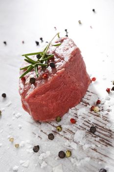 Big raw steak with peppercorns, garlic and fresh rosemary herbs on white wooden kitchen table. Culinary steak eating.
