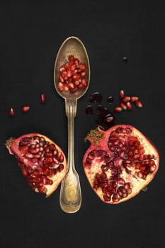 Delicious ripe pomegranate seeds with silver spoon on black background, top view. Healthy exotic fruit eating.