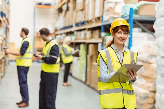Smiling warehouse manager holding clipboard in a large warehouse