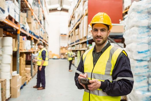 Smiling worker wearing yellow vest using handheld in a large warehouse