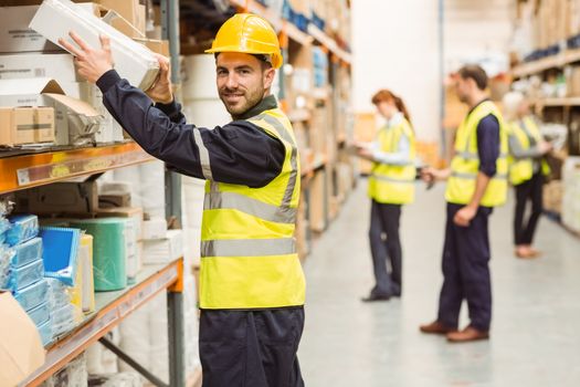 Smiling warehouse worker taking package in the shelf in a large warehouse