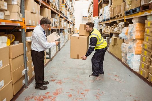 Manager watching worker carrying boxes in a large warehouse