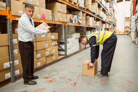 Manager watching worker carrying boxes in a large warehouse