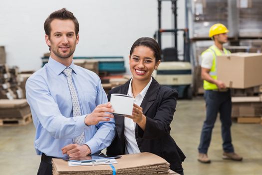 Warehouse managers showing box to camera in a large warehouse