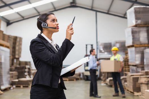 Warehouse manager wearing headset checking inventory in a large warehouse