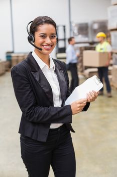 Warehouse manager wearing headset holding clipboard in a large warehouse