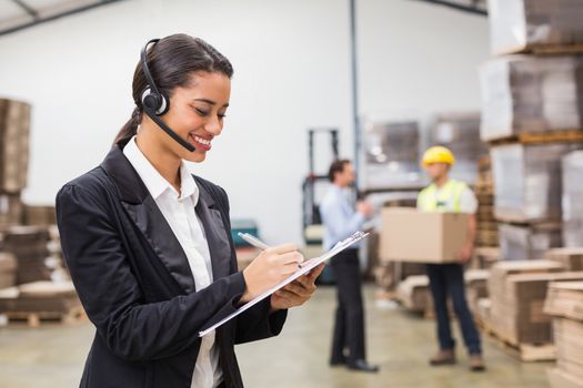 Warehouse manager writing on clipboard in warehouse