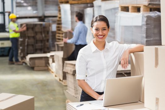 Smiling warehouse manager using laptop in a large warehouse