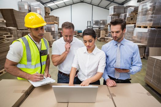 Warehouse managers and worker looking at laptop in a large warehouse