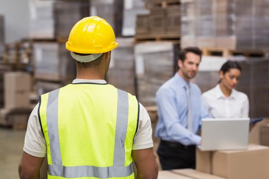 Rear view of warehouse worker in front of his managers in a large warehouse