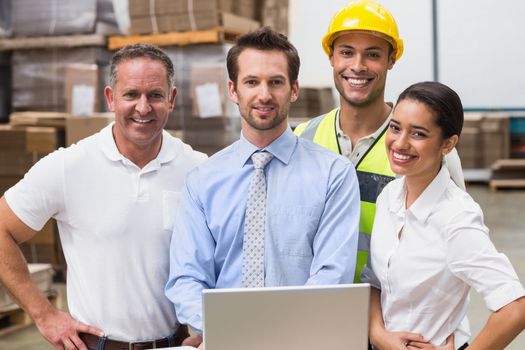 Warehouse managers and worker smiling at camera in a large warehouse