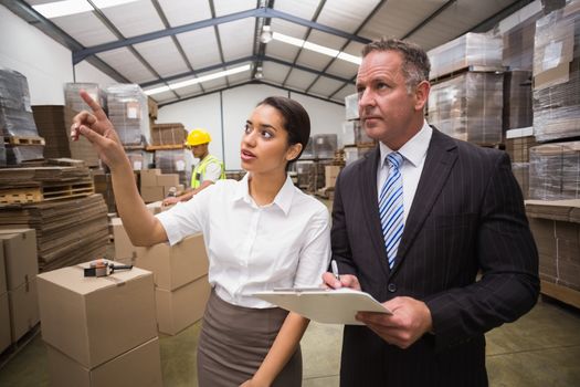 Warehouse manager showing something to her boss in a large warehouse