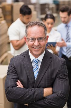 Boss wearing eyeglasses standing with arms crossed in a large warehouse