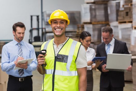 Worker standing with scanner in front of his colleagues in a large warehouse