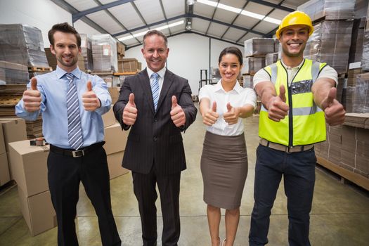 Warehouse team smiling at camera showing thumbs up in a large warehouse