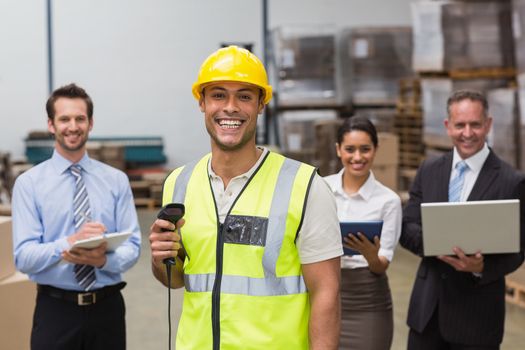 Worker standing with scanner in front of his colleagues in a large warehouse