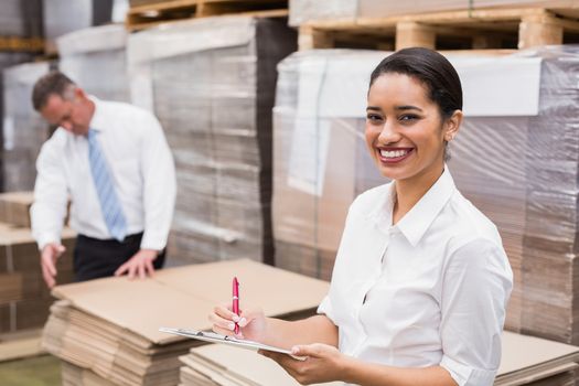 Warehouse manager writing on clipboard in warehouse