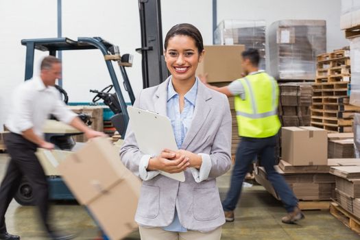 Portrait of smiling female manager holding files during busy period in warehouse