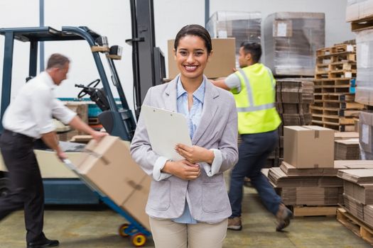 Portrait of smiling female manager holding files during busy period in warehouse
