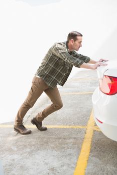 Man pushing his broken down car in a car park